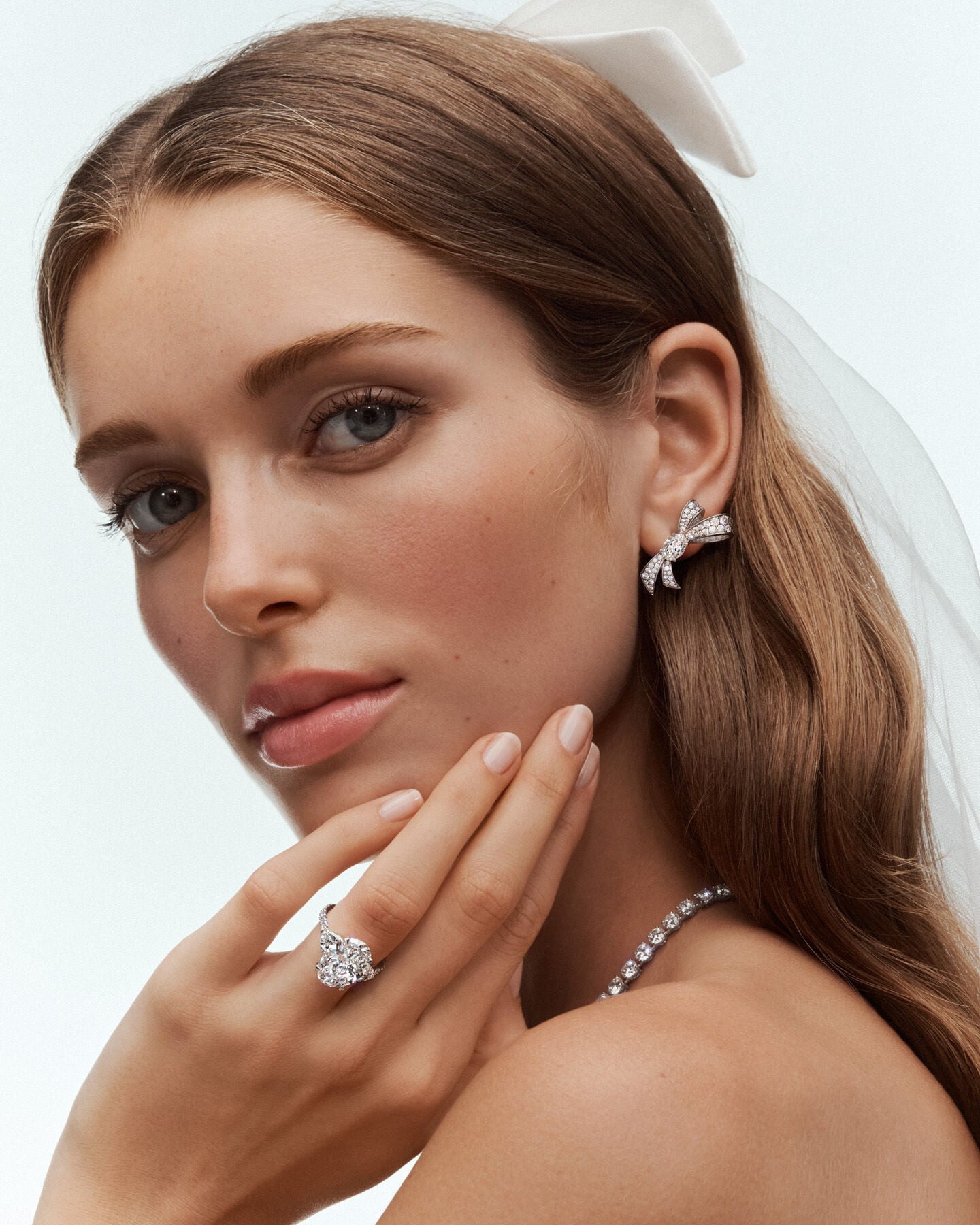 Bride wearing an Arvelle diamond bow ear climber, pear and round diamond engagement ring, and diamond tennis necklace